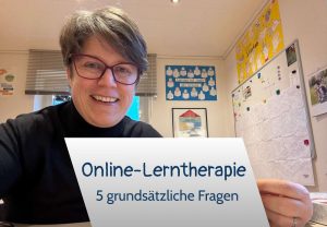 Sabine Landua in ihrer Lerntherapiepraxis hält ein Schild. Text: Online-Lerntherapie 5 Fragen