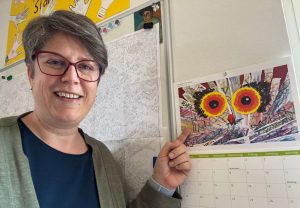 Sabine Landua zeigt auf ein Jalenderbild mit zwei großen Augen (vermutlich eine Eule)