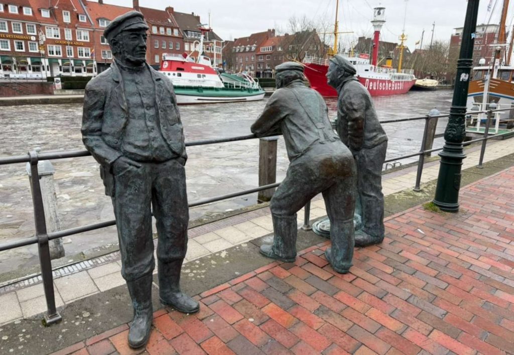 Emder Delftspucker Skulpturen, im Hintergrund Schiffe im Hafen